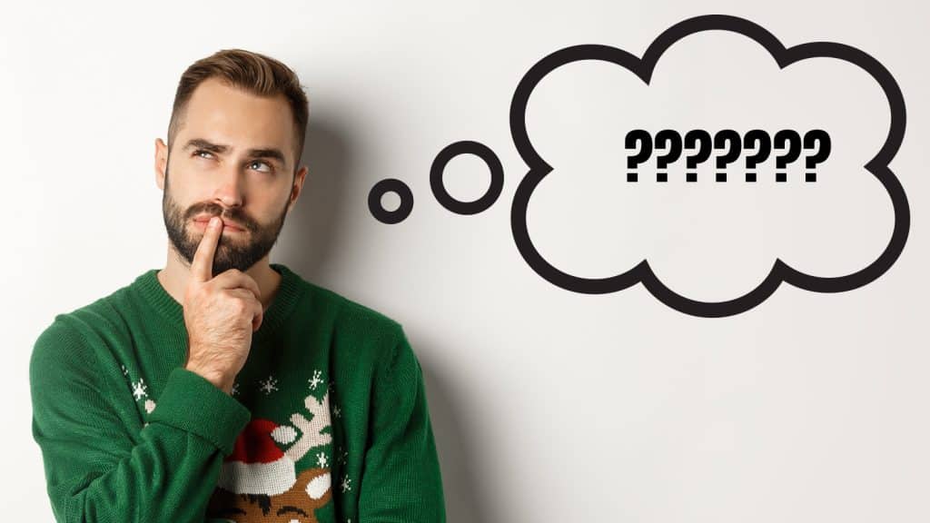 Hombre pensativo con jersey navideño verde reflexionando sobre qué regalar en Navidad