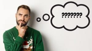 Hombre pensativo con jersey navideño verde reflexionando sobre qué regalar en Navidad